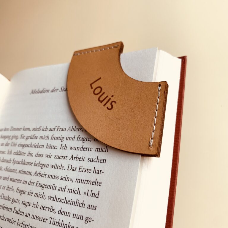 Lesezeichen aus Leder mit einer Gravur. Das Lesezeichen ist auf eine Buchseite gesteckt.